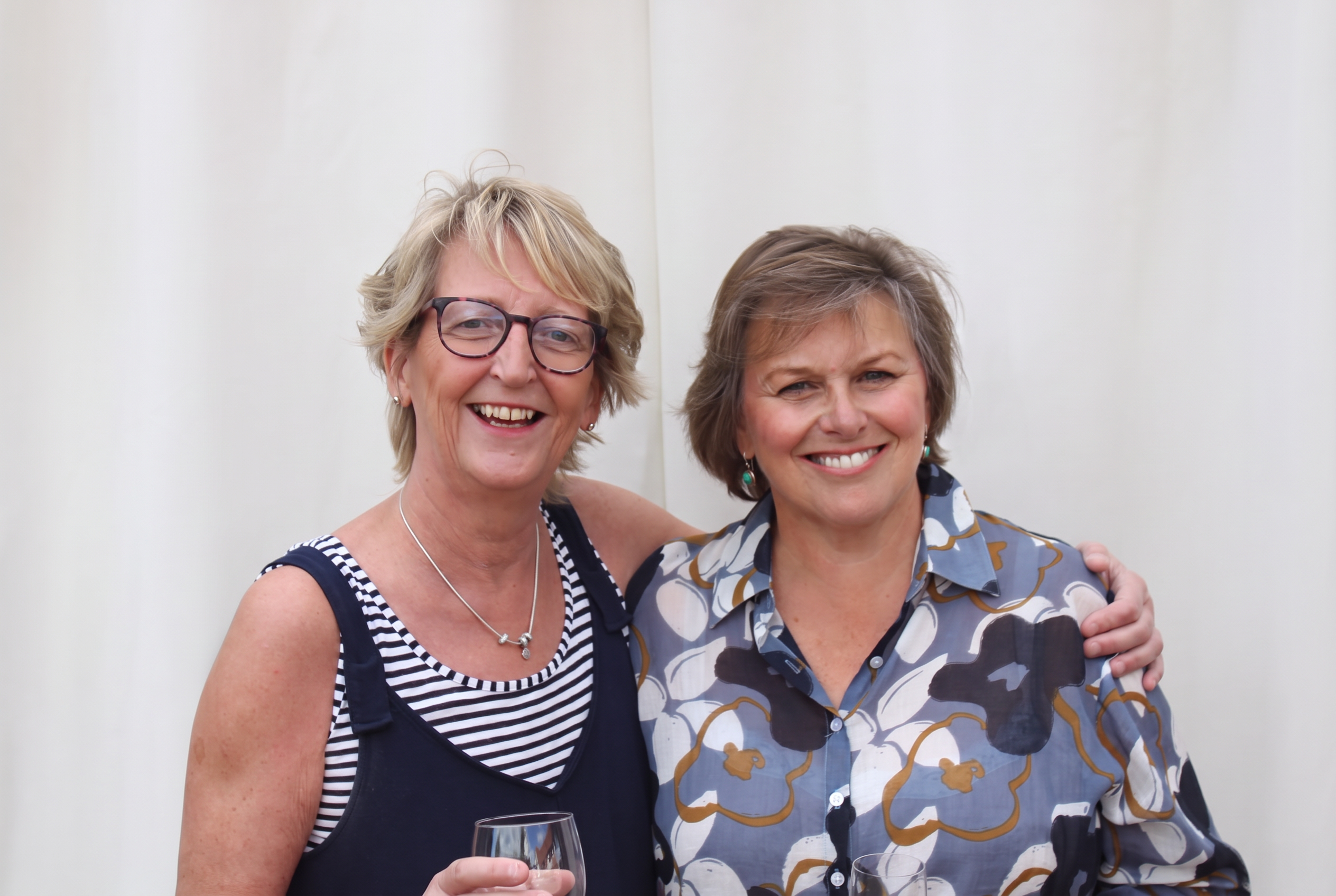 Two guests smiling together with wine glasses in front of the photo booth curtain