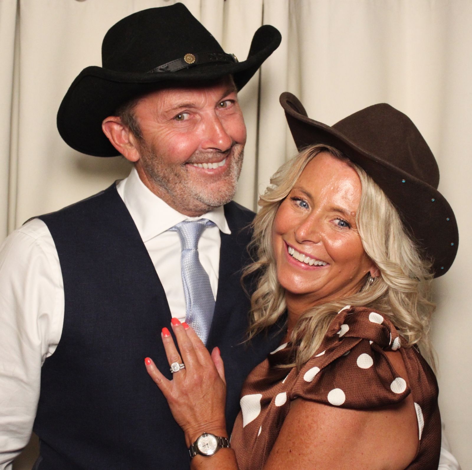 A couple in cowboy hats showing off a diamond ring at the photo booth