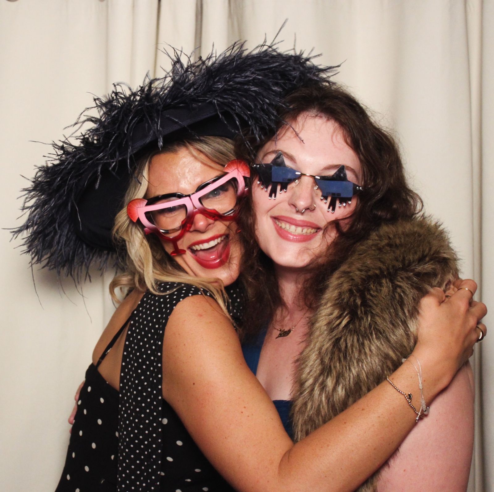Two women wearing a feathered hat and novelty sunglasses at the photo booth