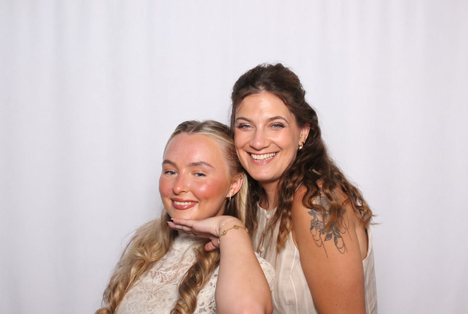 Two guests smiling cheek to cheek against the white curtain backdrop