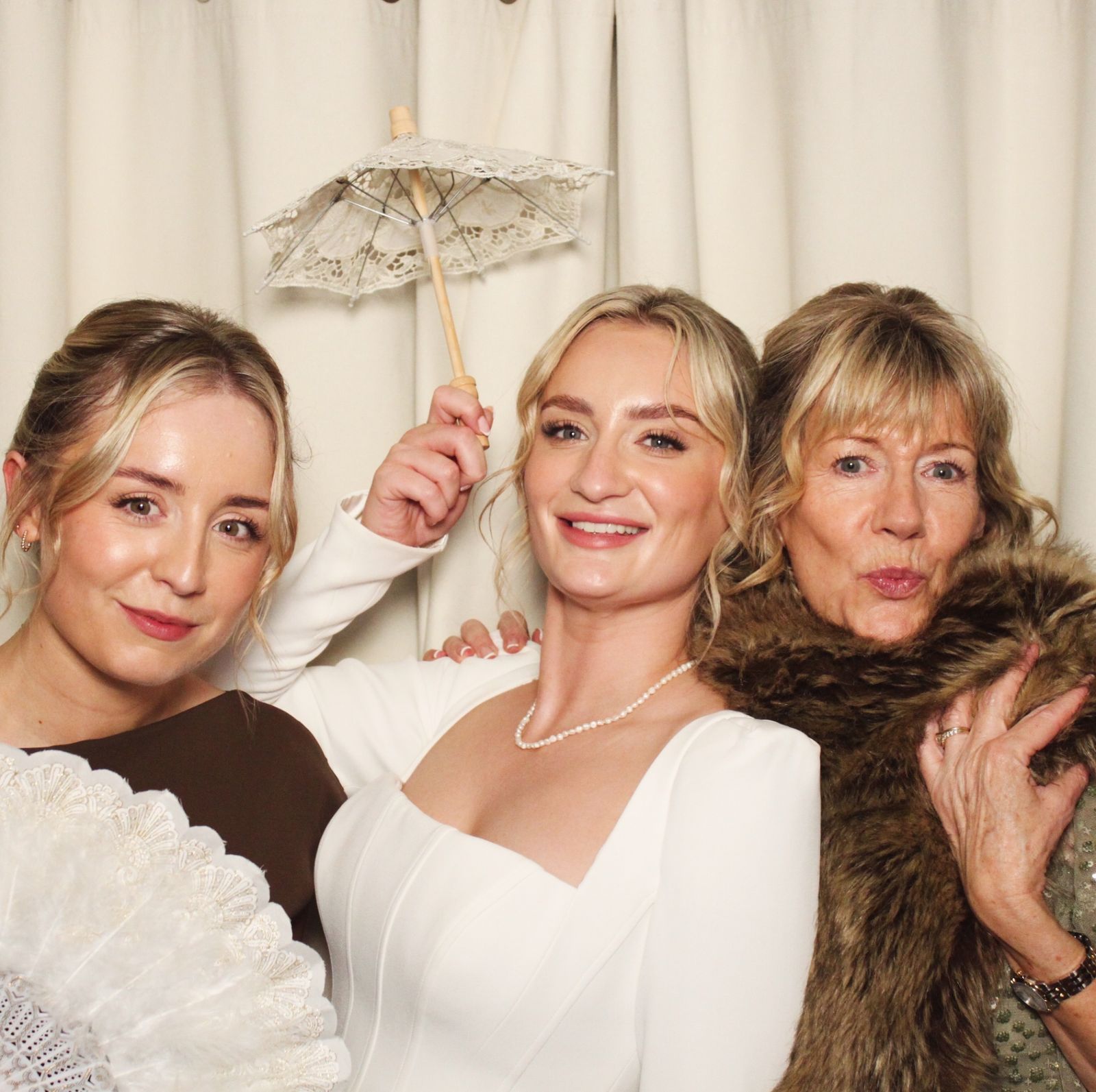 Three women posing with a lace parasol, fan and faux fur wrap at the photo booth