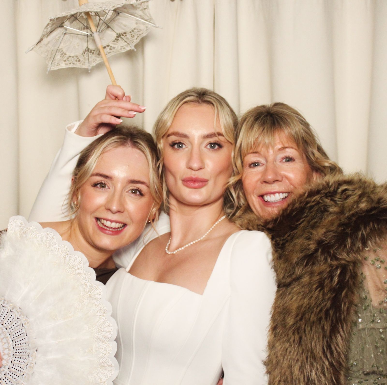 Three women posing with a parasol and props at the photo booth