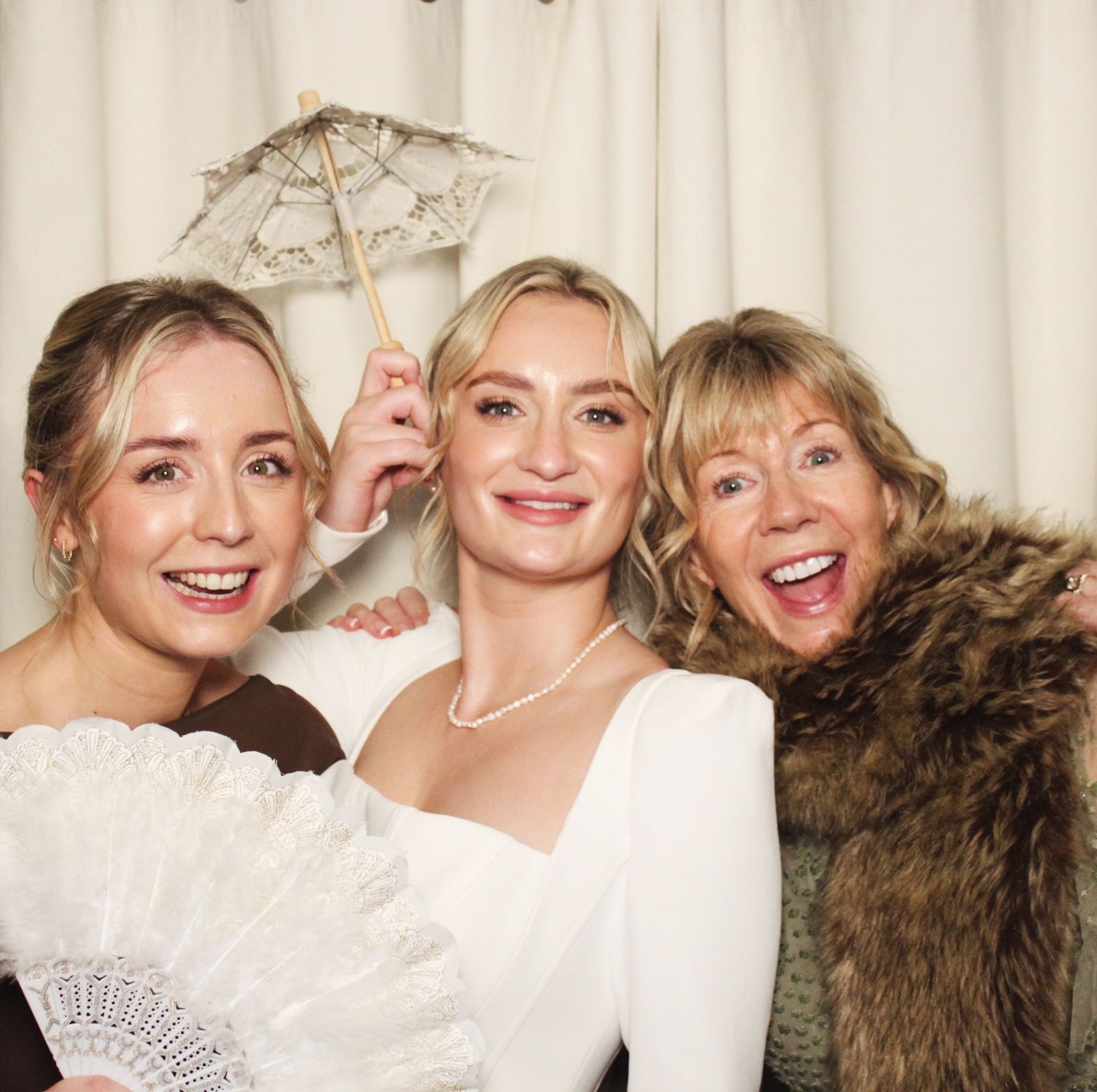 Three women smiling broadly together with props at the photo booth