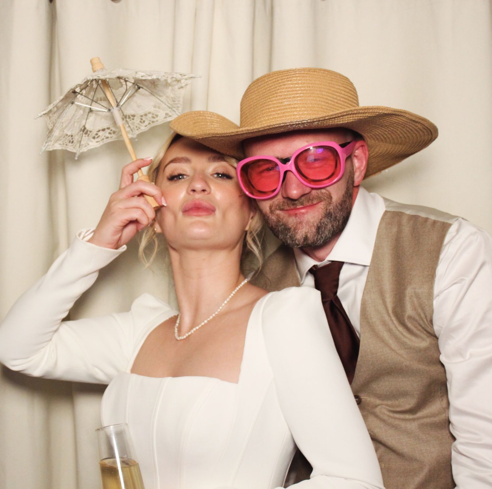 A woman with a lace parasol and a man in a straw hat and pink sunglasses at the photo booth
