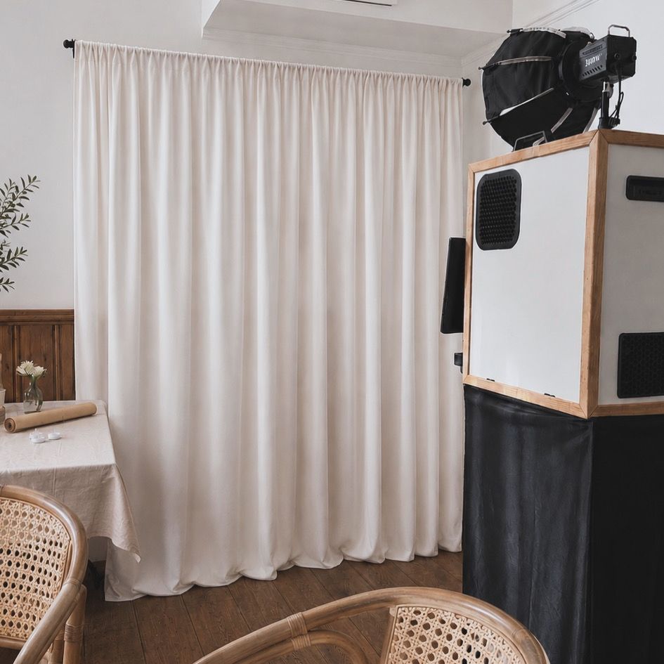 Freestanding photo booth setup with cream curtain backdrop and rattan seating