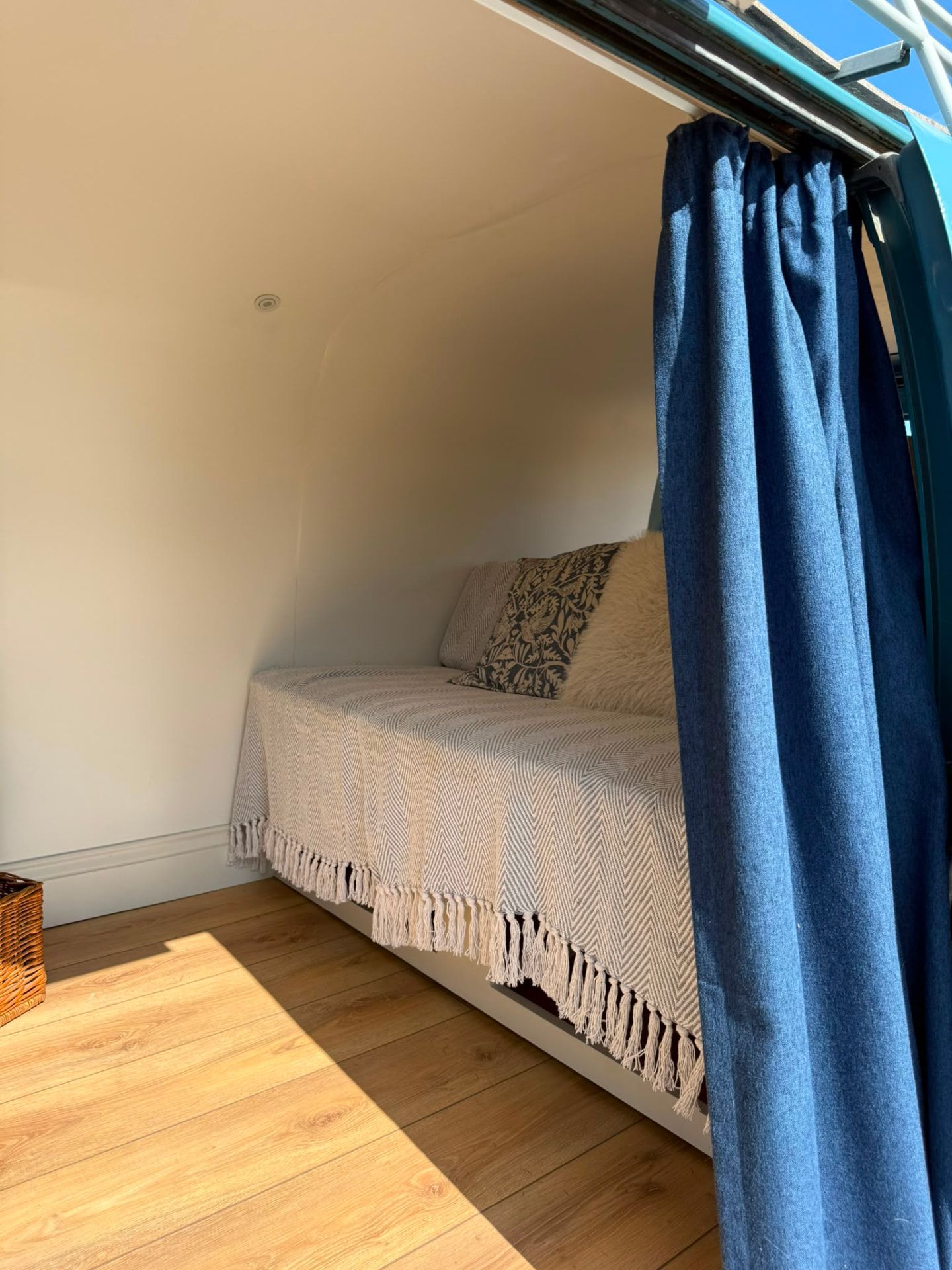 Inside the VW camper photo booth with a cream throw, cushions and denim curtain