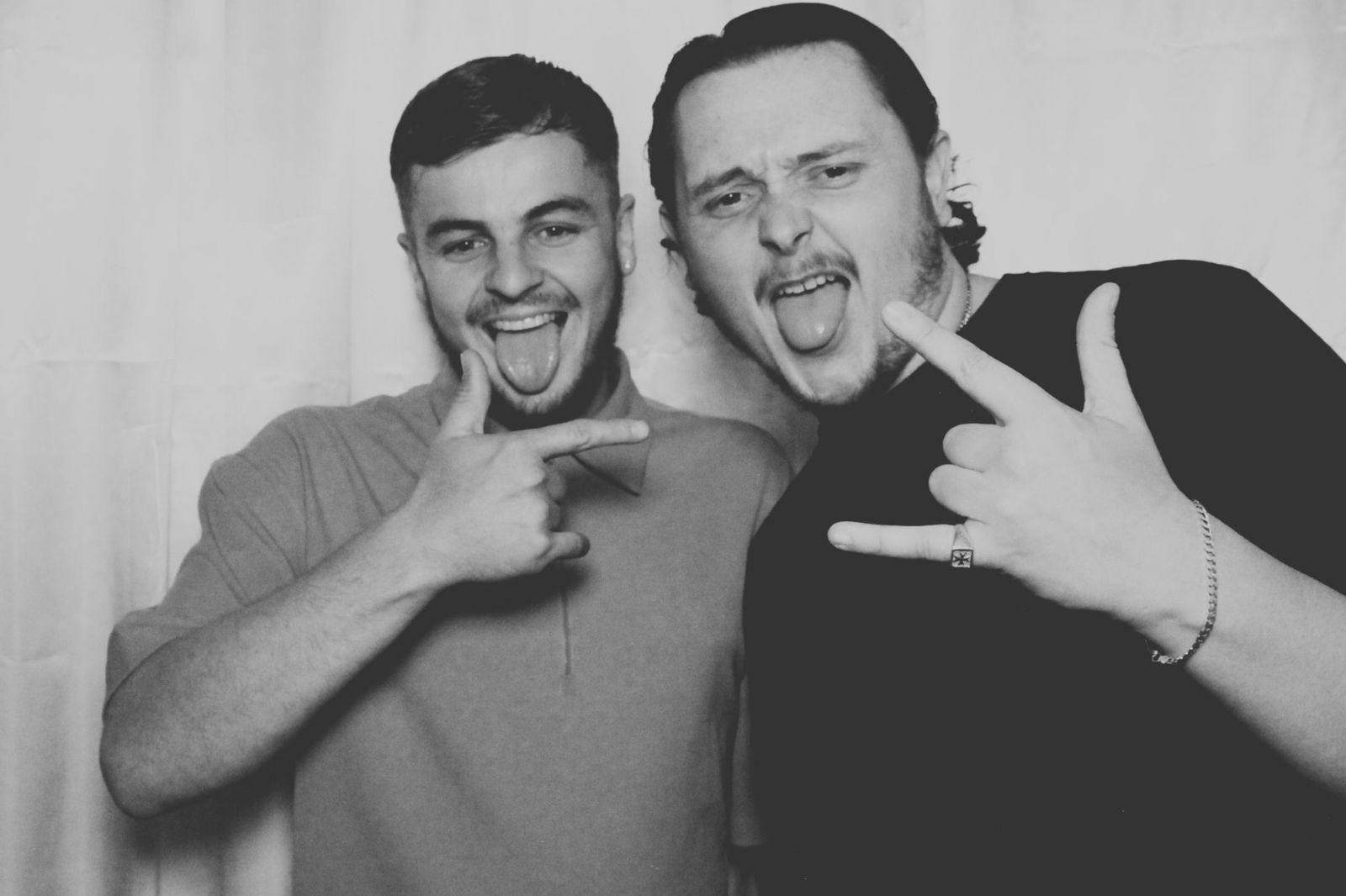 Two friends pulling funny faces and peace signs in the photo booth