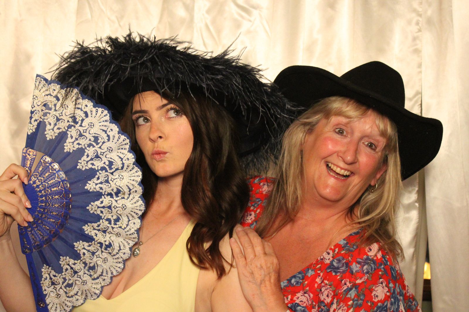 Two guests posing with a blue lace fan and feathered hats at Hunt Gathering