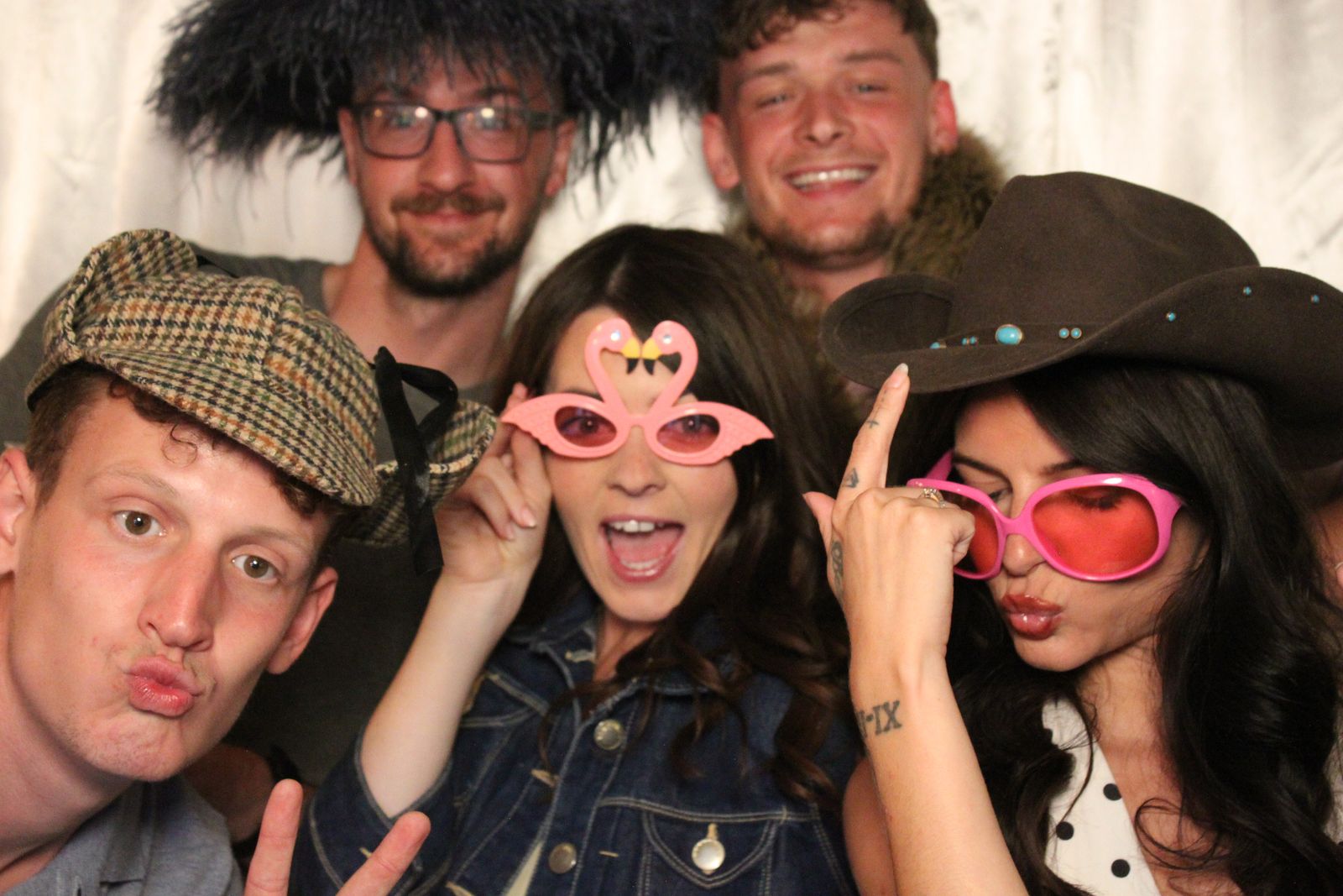 Group of five friends in hats and novelty glasses posing in the booth