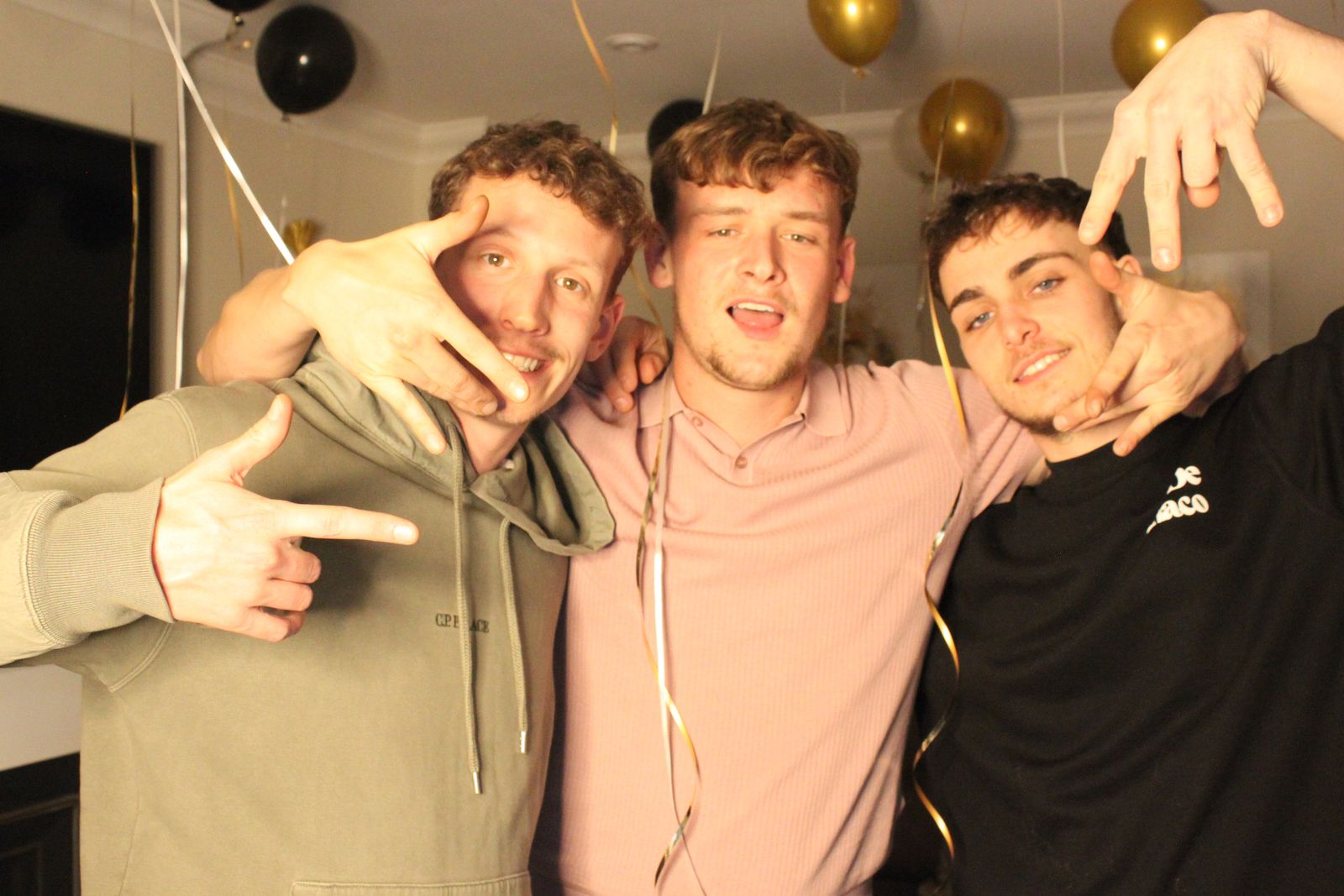 Three friends posing with peace signs at a New Year's Eve party with black and gold balloons