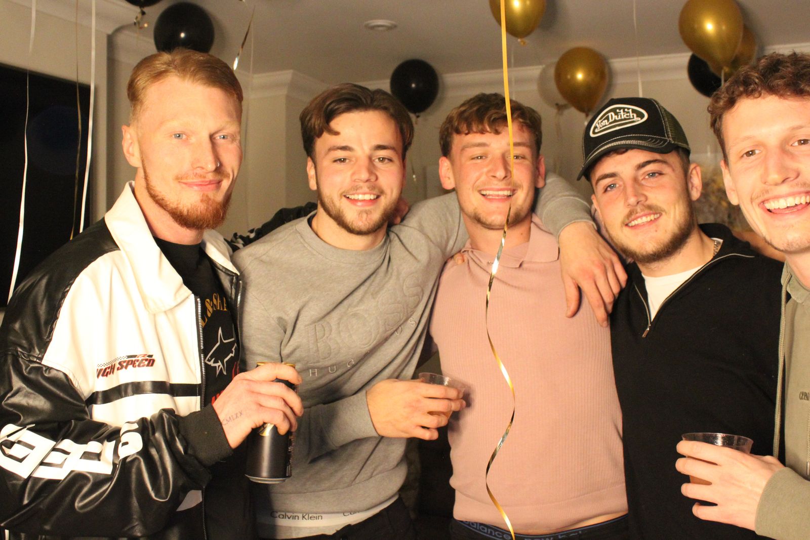 Five friends smiling together with drinks at a New Year's Eve party