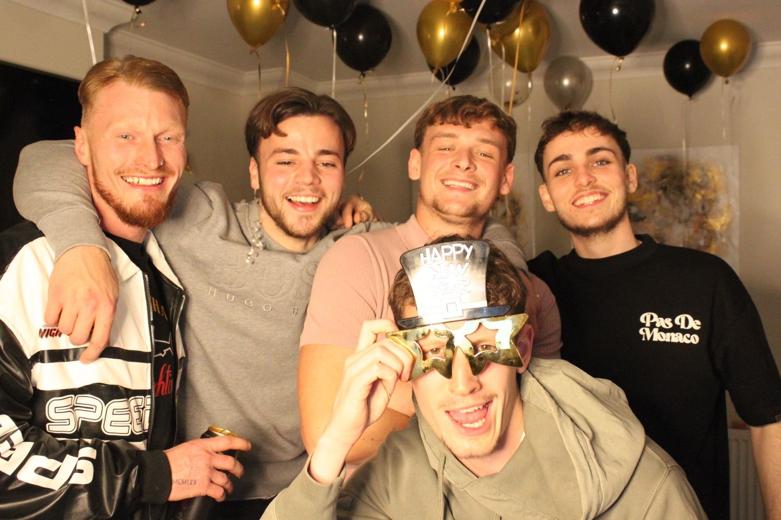 Group of friends laughing with Happy New Year novelty glasses and gold balloons