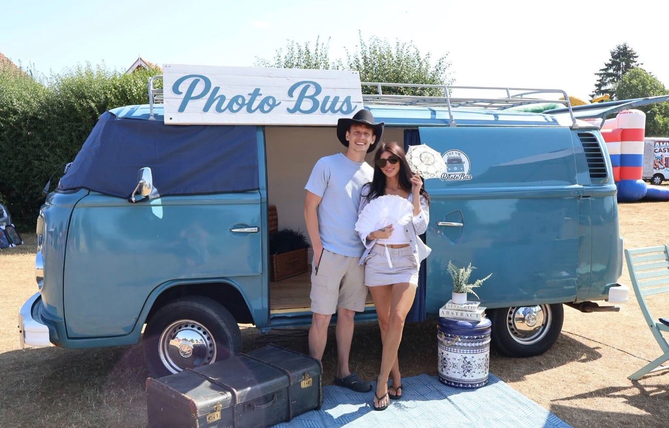 Couple posing with props in front of Stitch, the 1979 VW Type 2 Camper photo booth, at an outdoor event