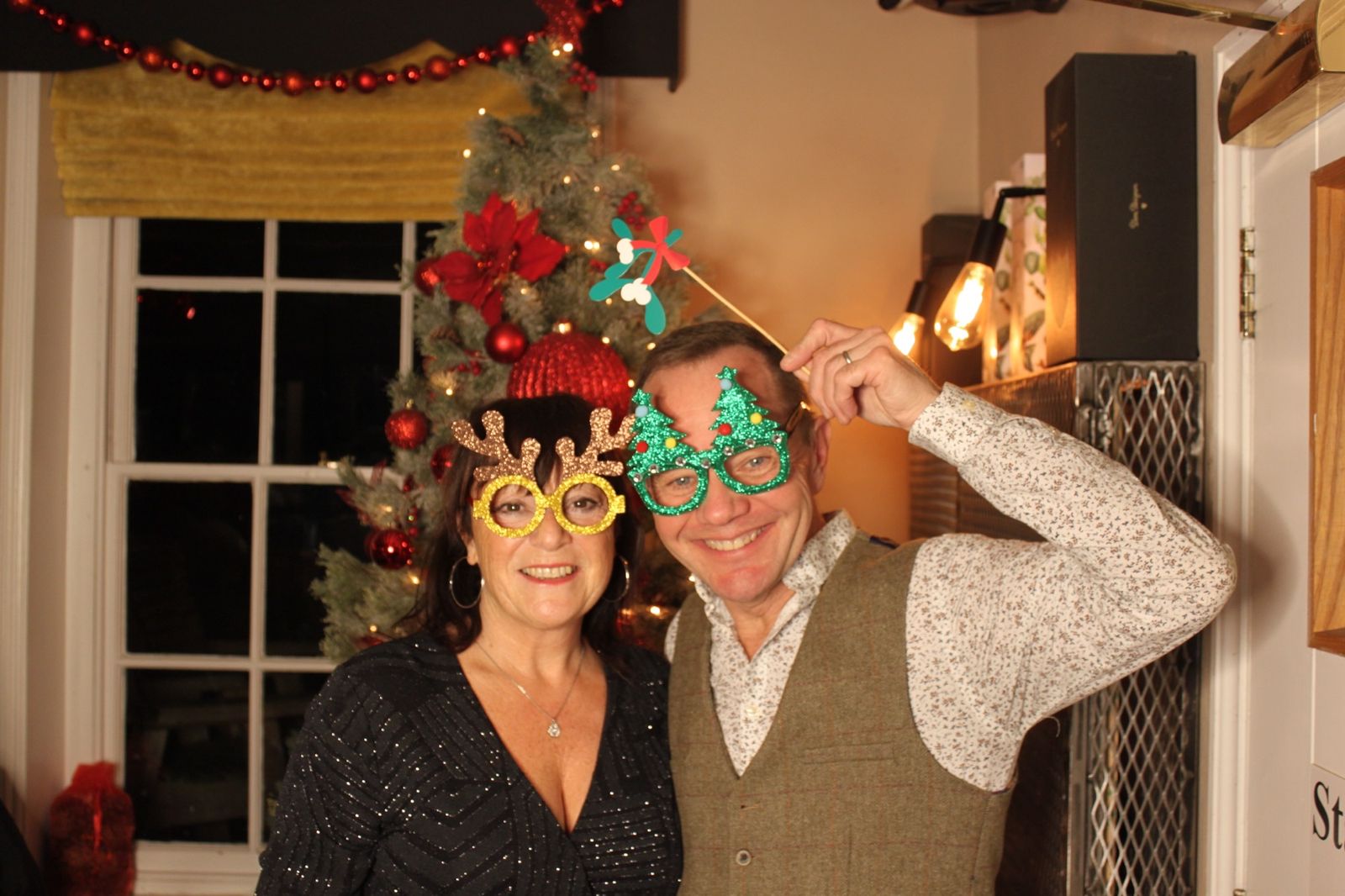 Couple wearing reindeer and Christmas tree glasses in front of a decorated tree