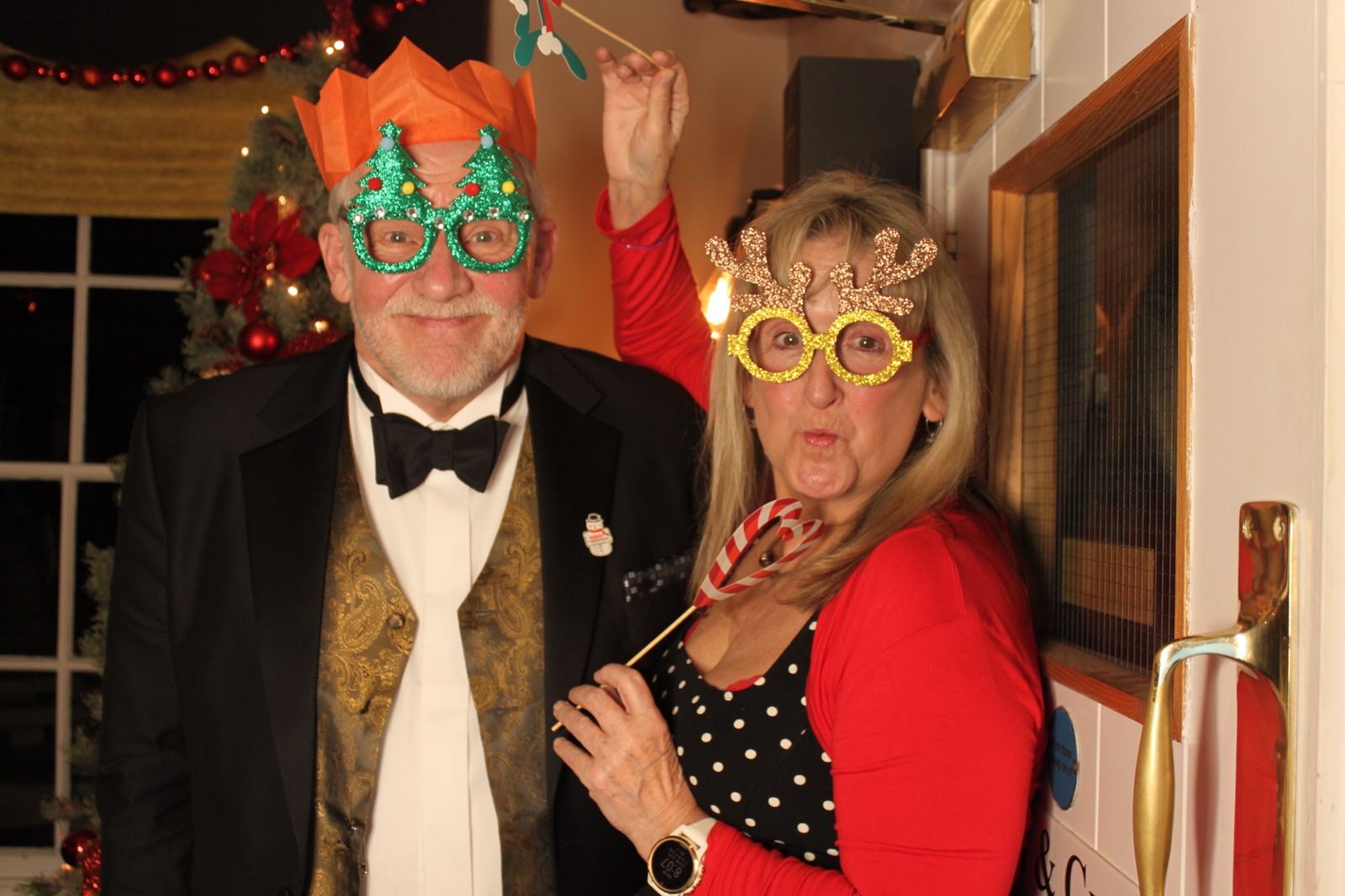 Guests in tuxedo and red dress wearing festive glasses and holding a candy cane